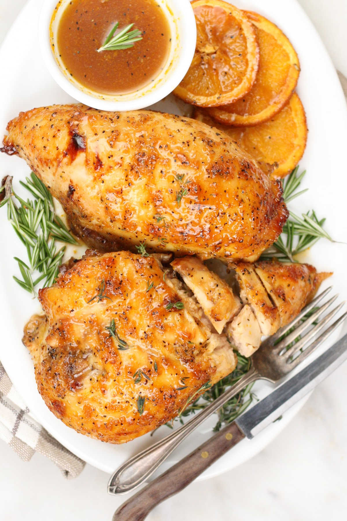 Roasted chicken breasts on an white oval plate with cooked orange slices.