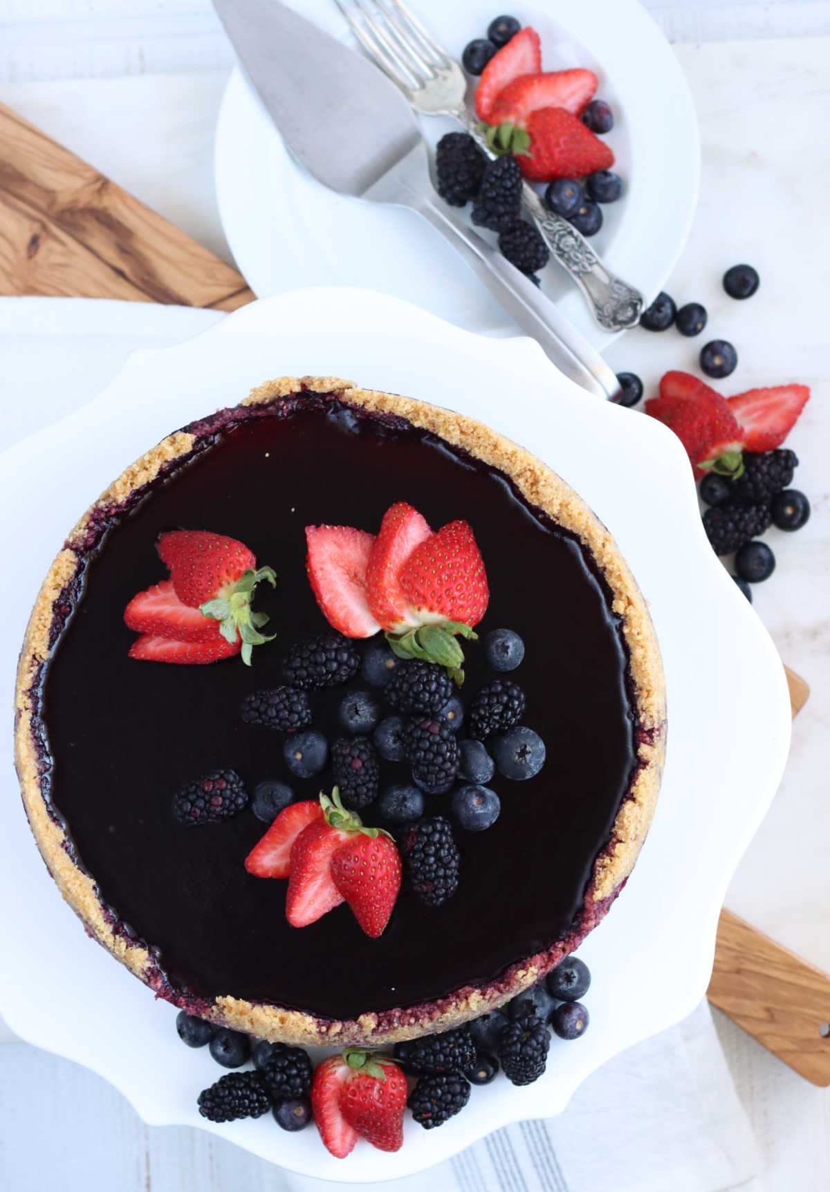 Cheesecake with berry topping and fresh berries on white footed cake dish.