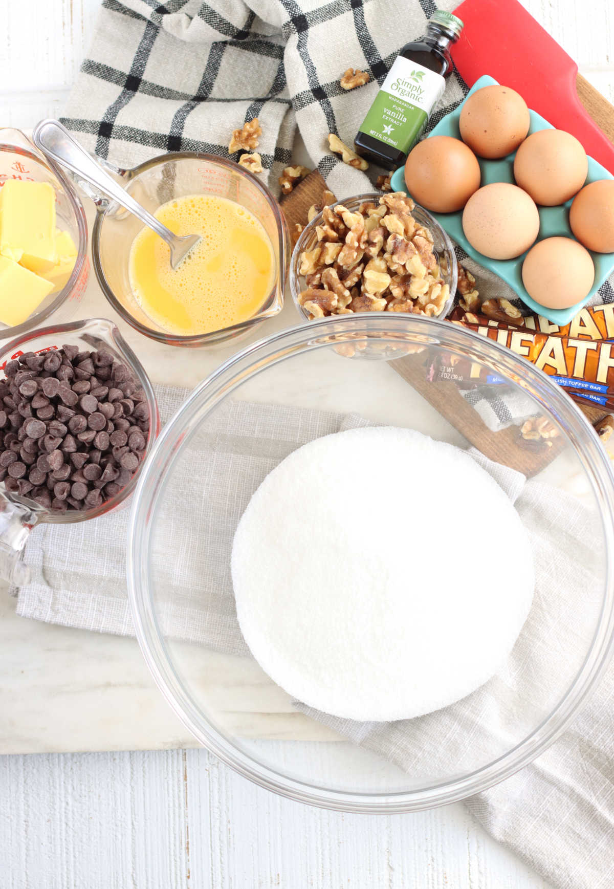 Ingredients for brownies, bowl of sugar, eggs, walnuts, glass measuring cups with chocolate chips and beaten eggs.