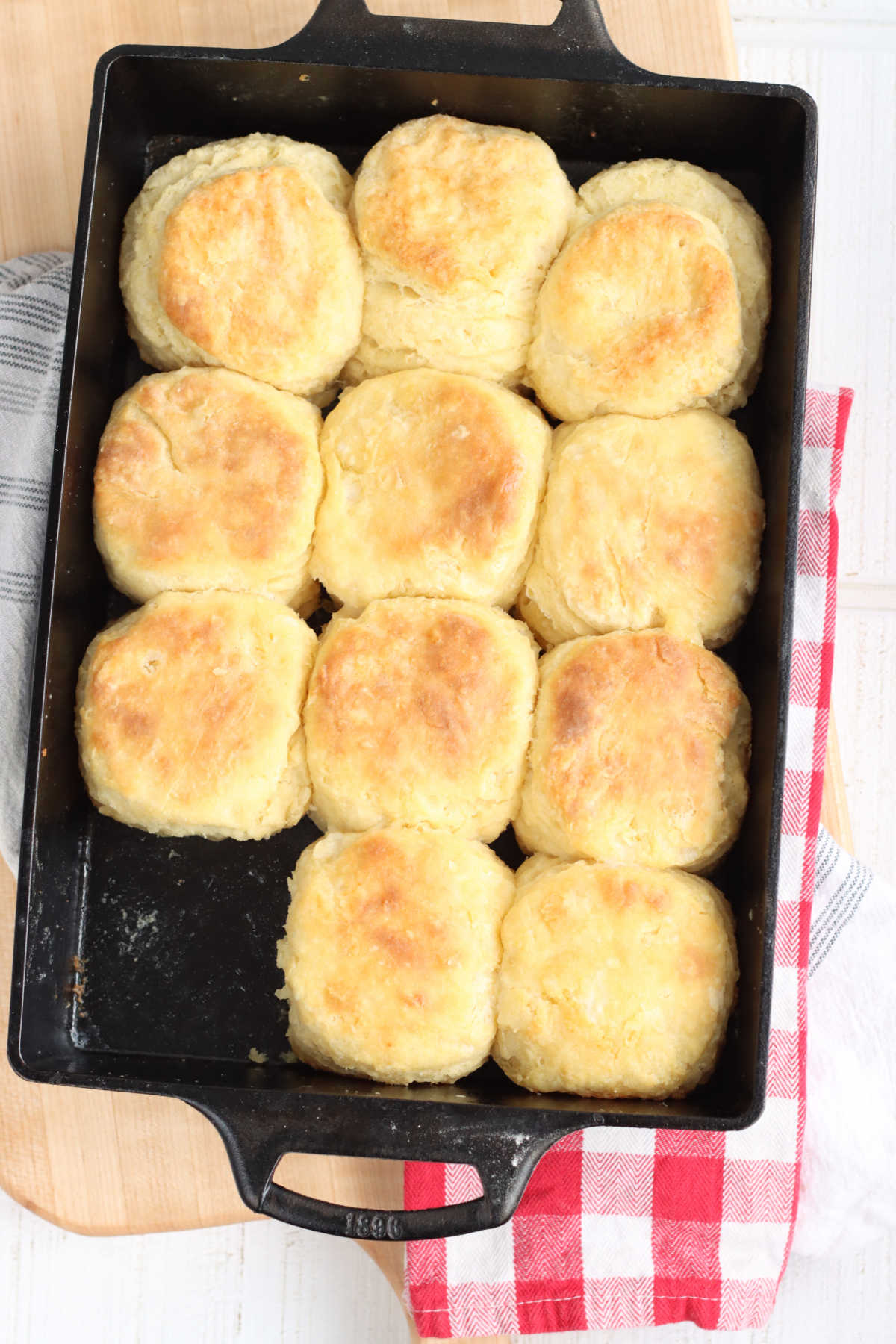 Homemade biscuits in rectangle cast iron pan on wooden cutting board, red and white checker cloth. 