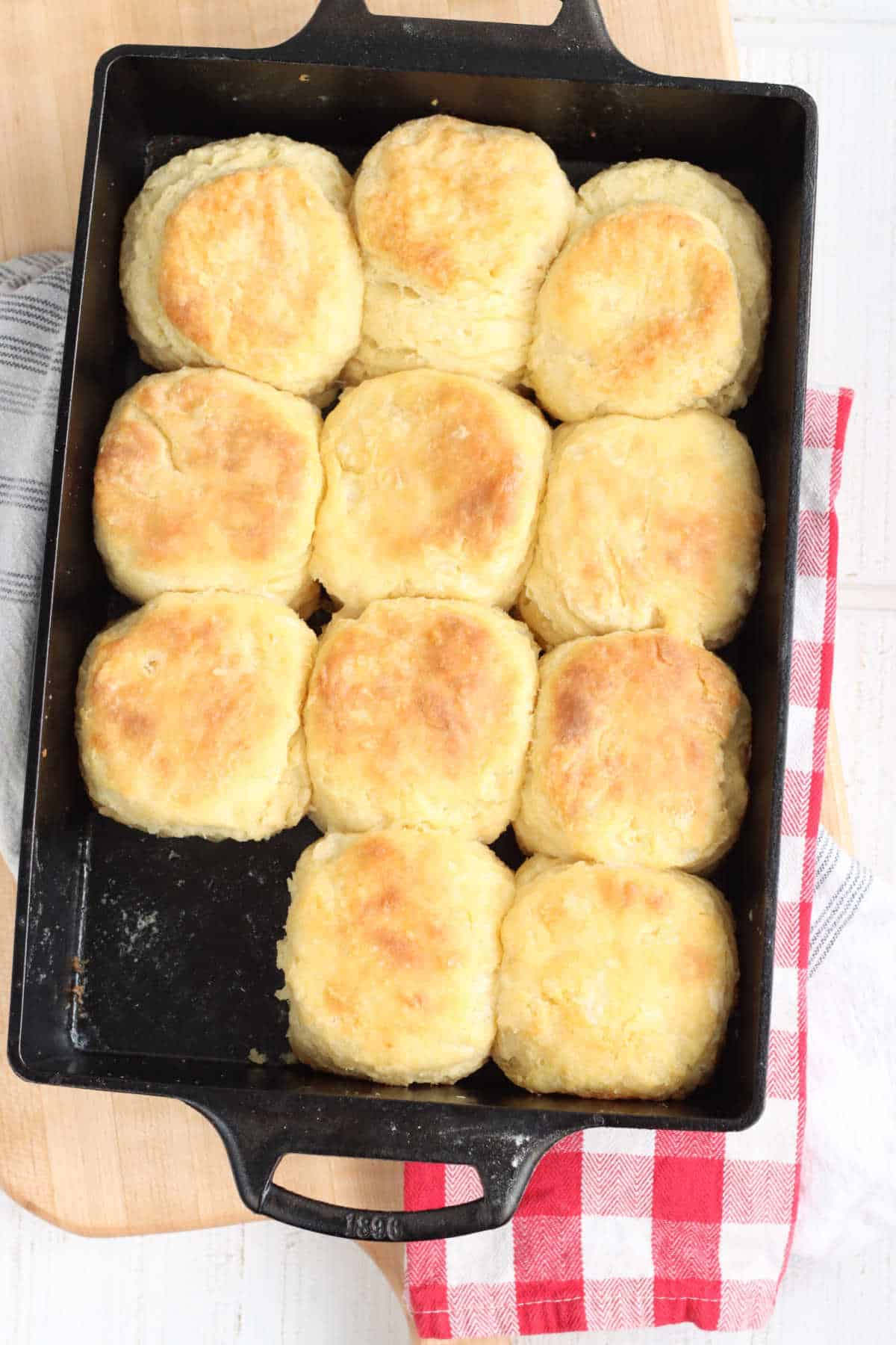 Homemade biscuits in rectangle cast iron pan on wooden cutting board, red and white checker cloth. 