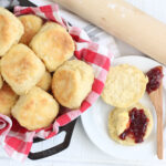 Biscuits in cast iron skillet, one in half on small white plate topped with raspberry jam.