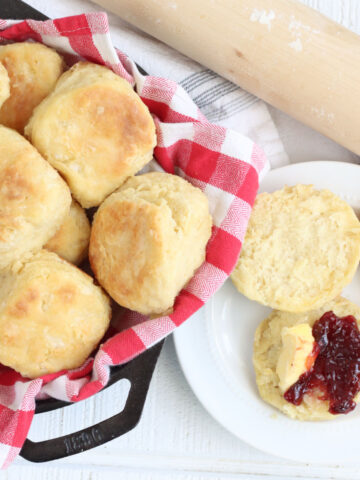 Biscuits in cast iron skillet, one in half on small white plate topped with raspberry jam.