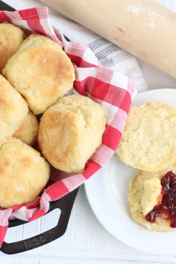 Biscuits in cast iron skillet, one in half on small white plate topped with raspberry jam.