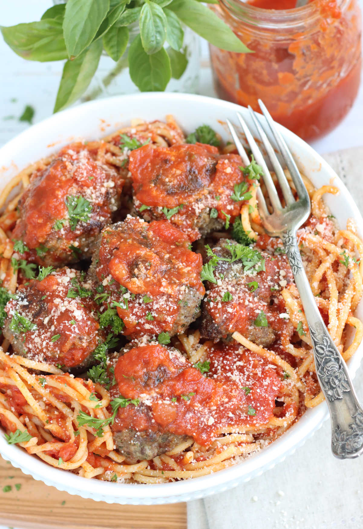 Spaghetti and meatballs in small white bowl with fork, sitting on wooden cutting board.