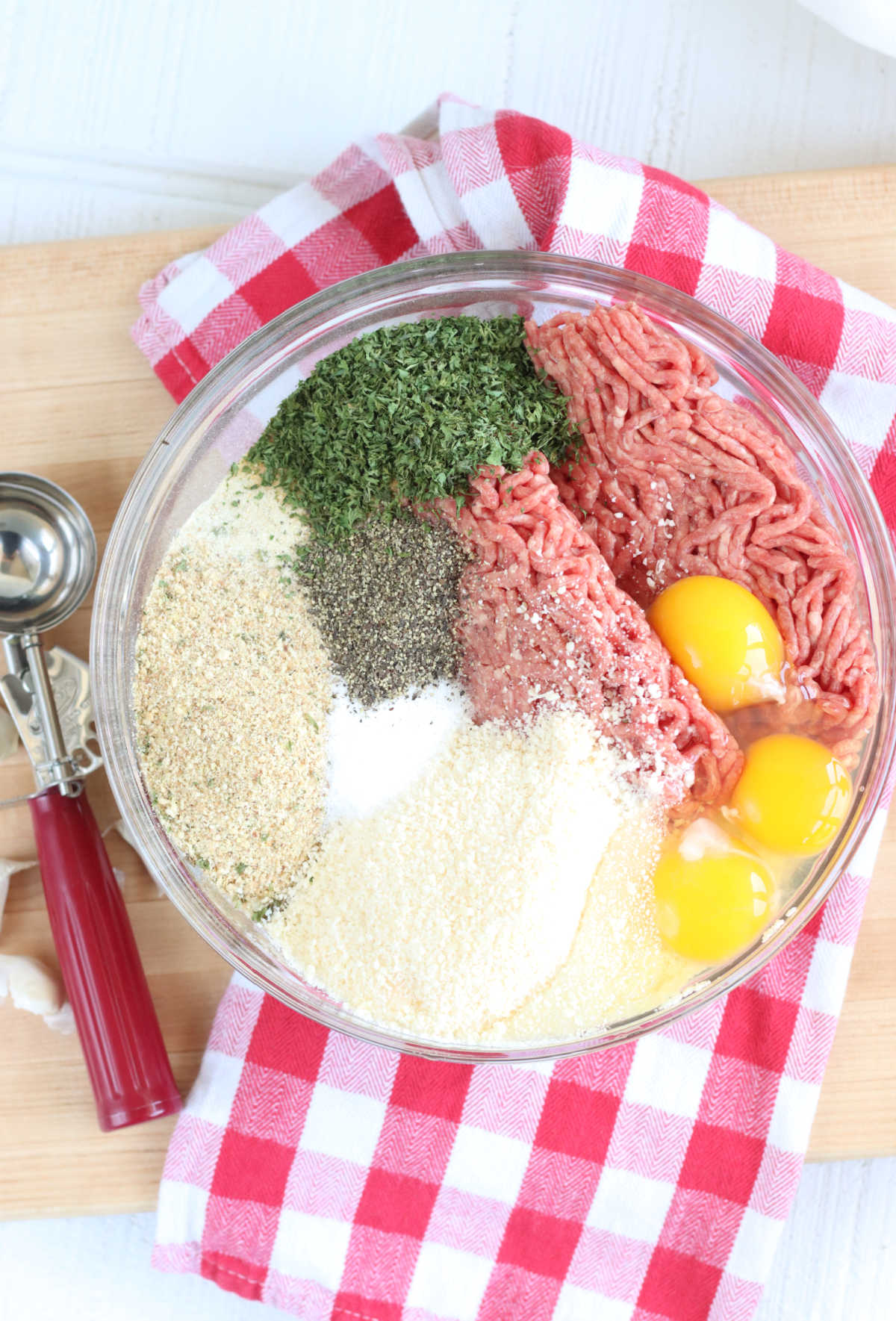 Clear glass bowl with ground beef, breadcrumbs, eggs, parsley, salt, pepper and Parmesan cheese.
