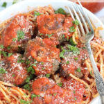 Meatballs with spaghetti and sauce in white bowl with fork.