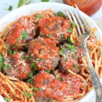 Meatballs in white bowl with spaghetti and pasta sauce.