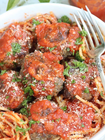 Meatballs in white bowl with spaghetti and pasta sauce.
