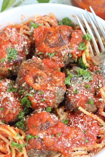 Meatballs in white bowl with spaghetti and pasta sauce.