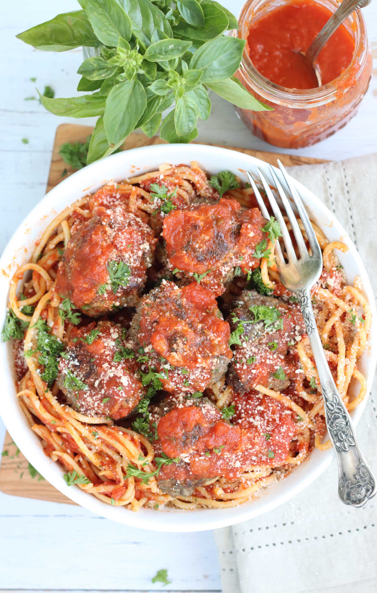 Spaghetti with meatballs in white bowl, fork to right, on wooden cutting board.