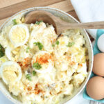 Bowl of potato salad with eggs on wooden cutting board.