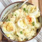Potato salad in light color bowl topped with slices of hard boiled eggs.