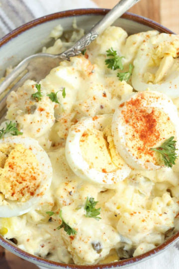 Potato salad in light color bowl topped with slices of hard boiled eggs.