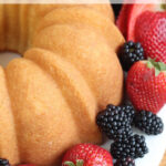 Bundt cake on white footed cake dish with fresh berries.