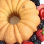 Pound cake on white footed cake dish surrounded by berries.