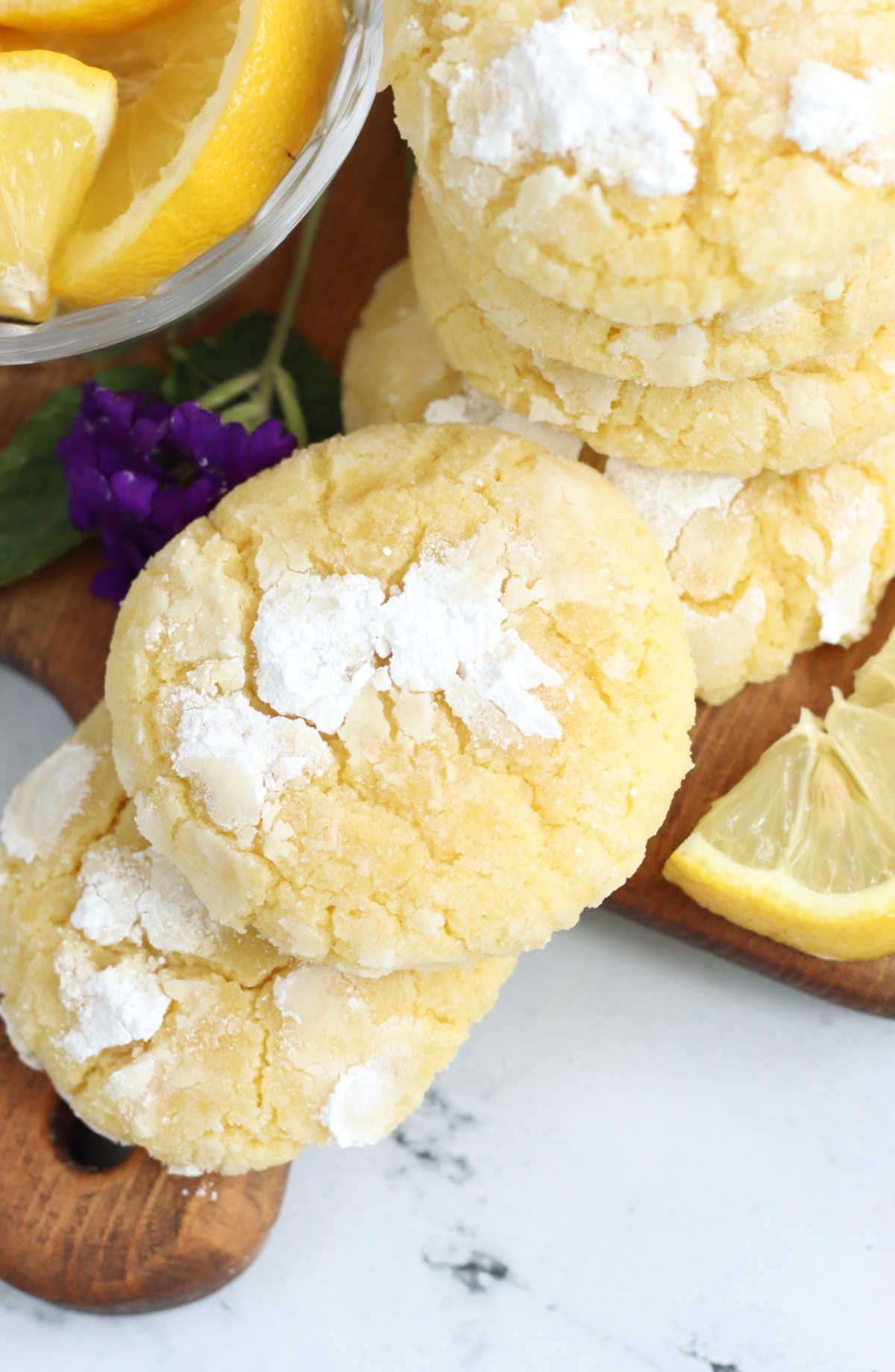 Lemon crinkle cookies stacked on wooden cutting board.