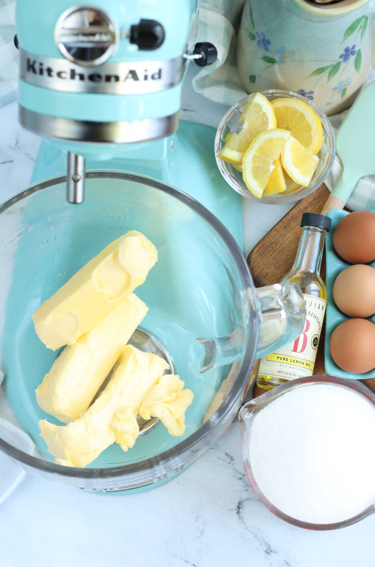Light teal stand mixer with glass bowl, butter and sugar.