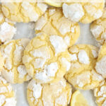 Lemon crinkle cookies on half sheet pan with lemon wedges.