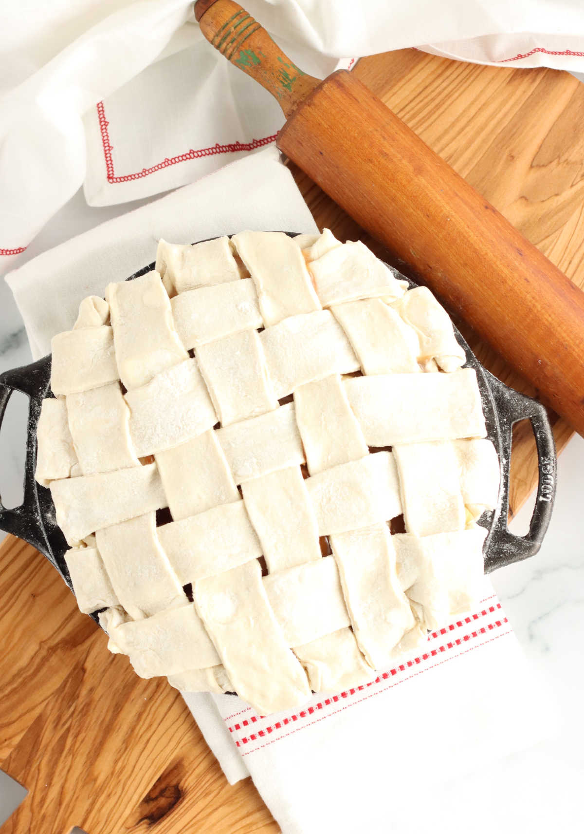 Lattice pie crust on unbaked pie in dual handle cast iron pan on wooden cutting board.