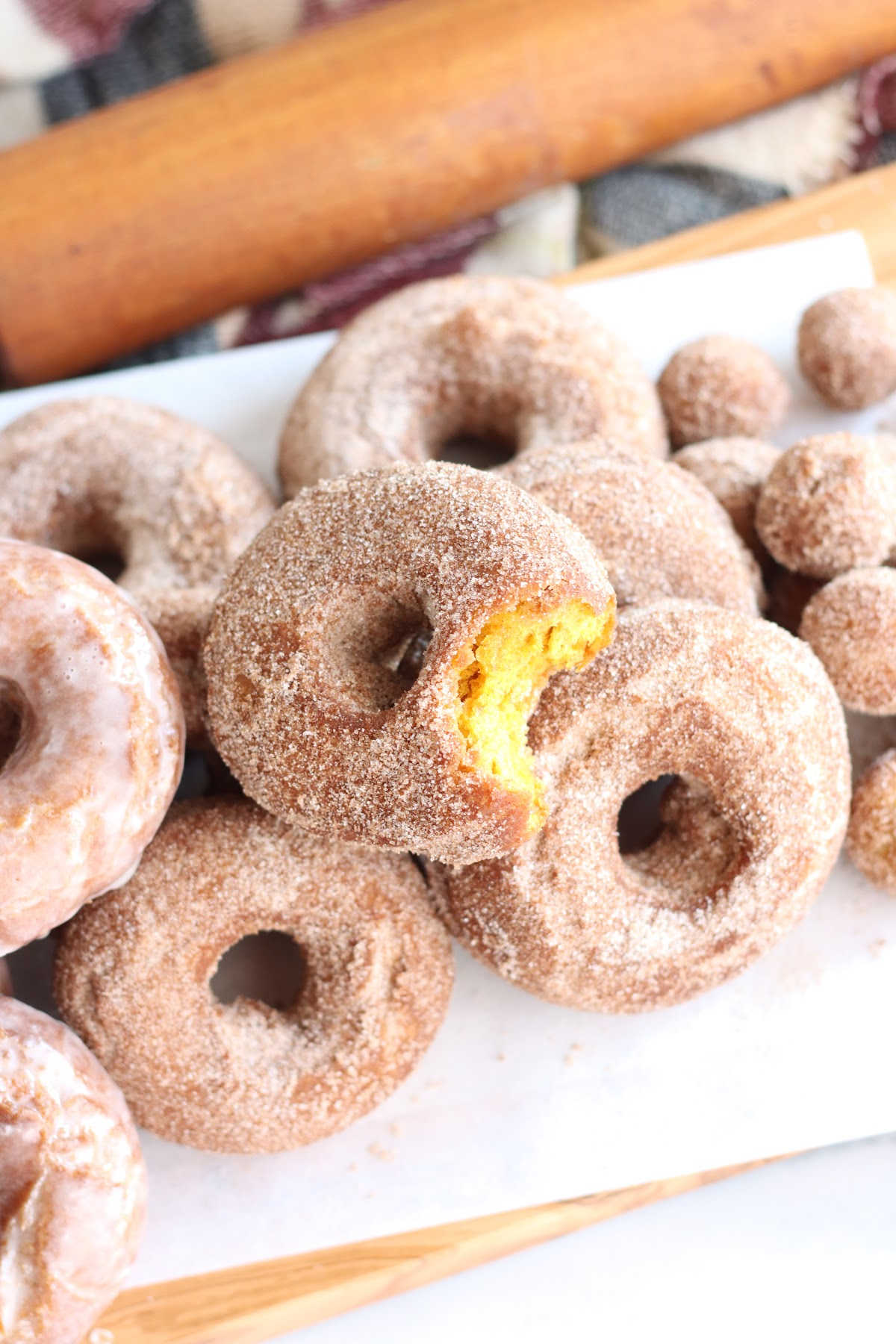 Pumpkin donuts with cinnamon sugar stacked on each other, one with bite.