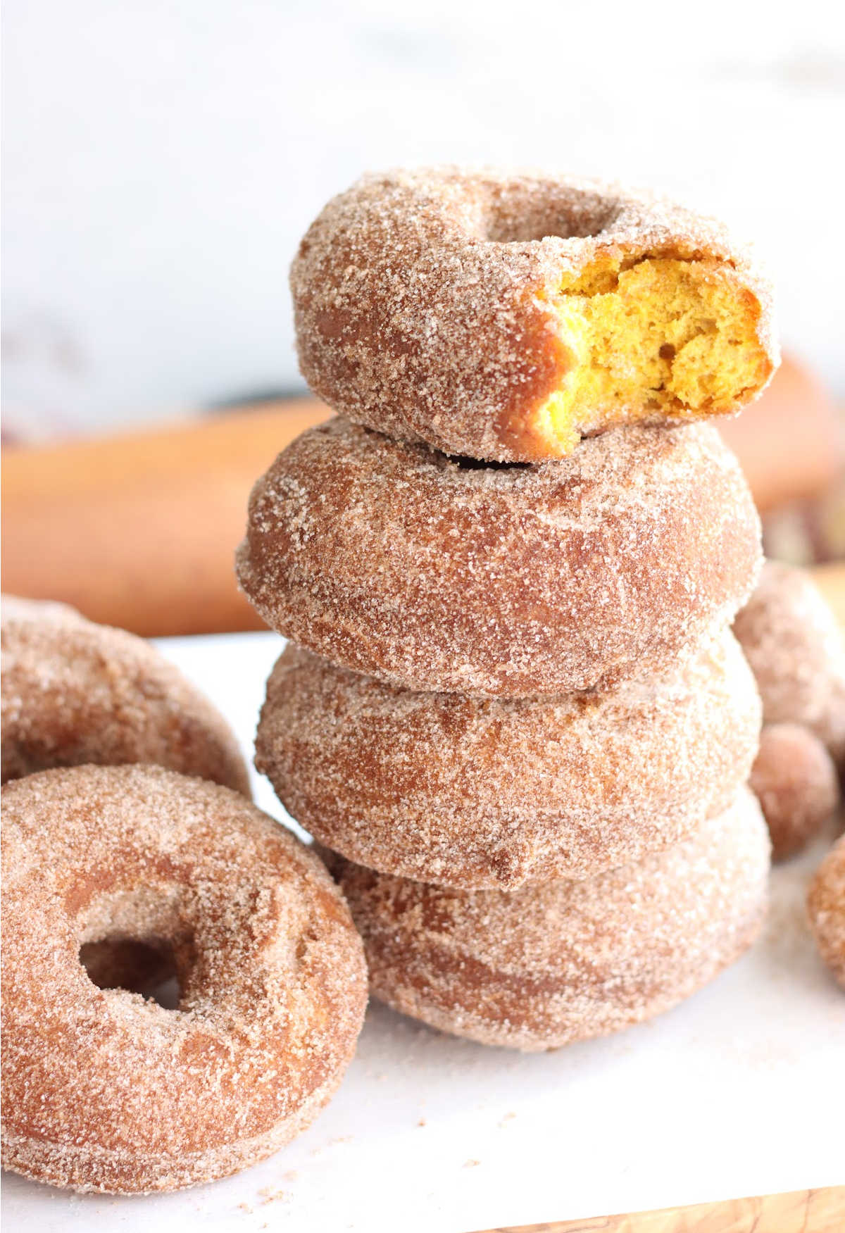 Pumpkin donuts stacked on each other with top one with bite out of it.