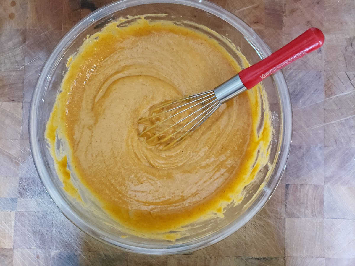 Mixed pumpkin cake batter with red handled whisk in clear glass bowl on butcher block.