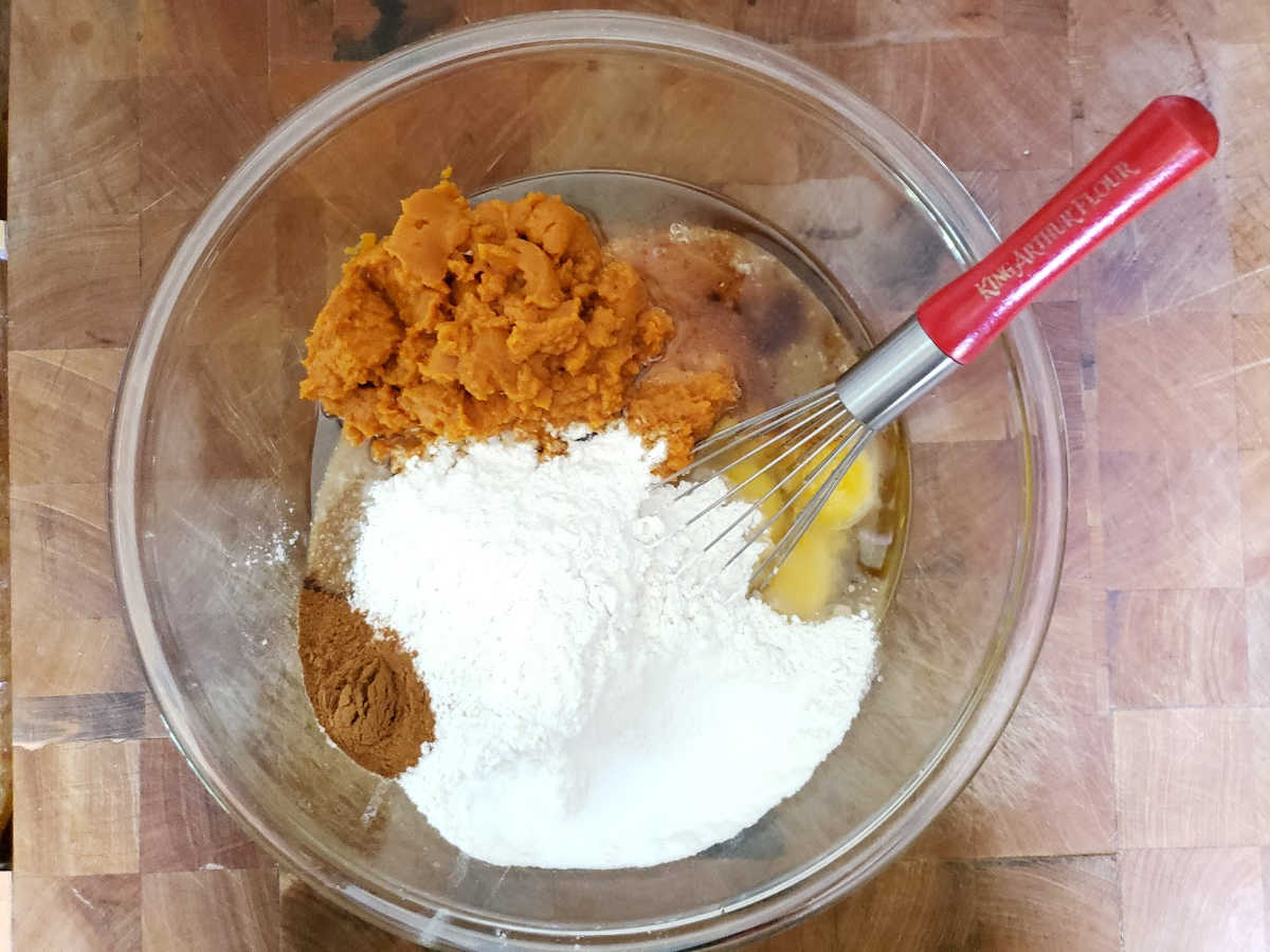 Batter ingredients for pumpkin cake in clear glass bowl on butcher block.