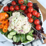 Small white plate with salad greens, scoop of tuna salad, cherry tomatoes, sliced cucumber, orange pepper.