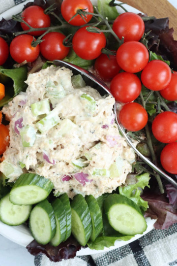 Small white plate with salad greens, scoop of tuna salad, cherry tomatoes, sliced cucumber, orange pepper.