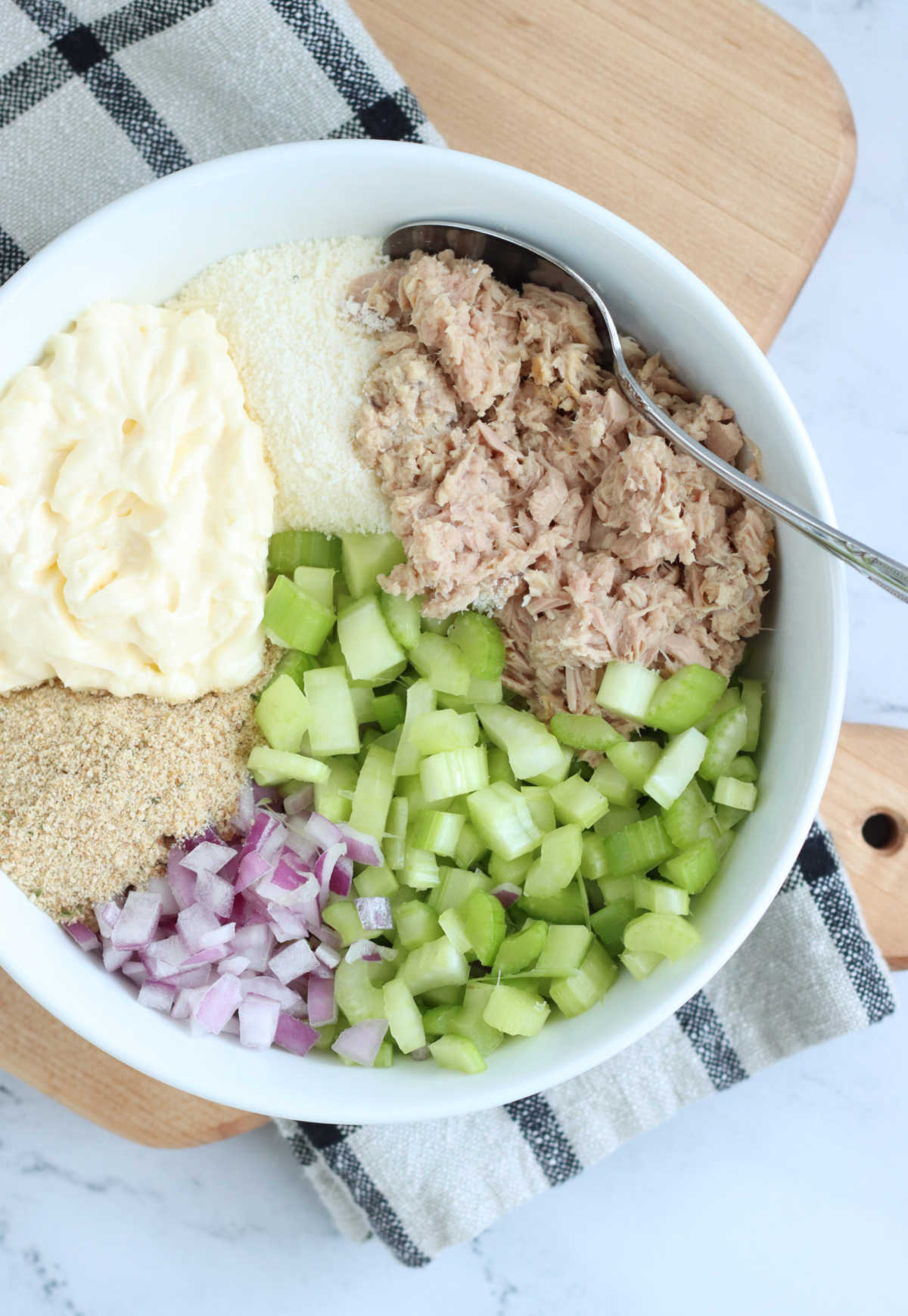 Small white bowl with chopped celery, red onion, mayonnaise, bread crumbs and tuna.
