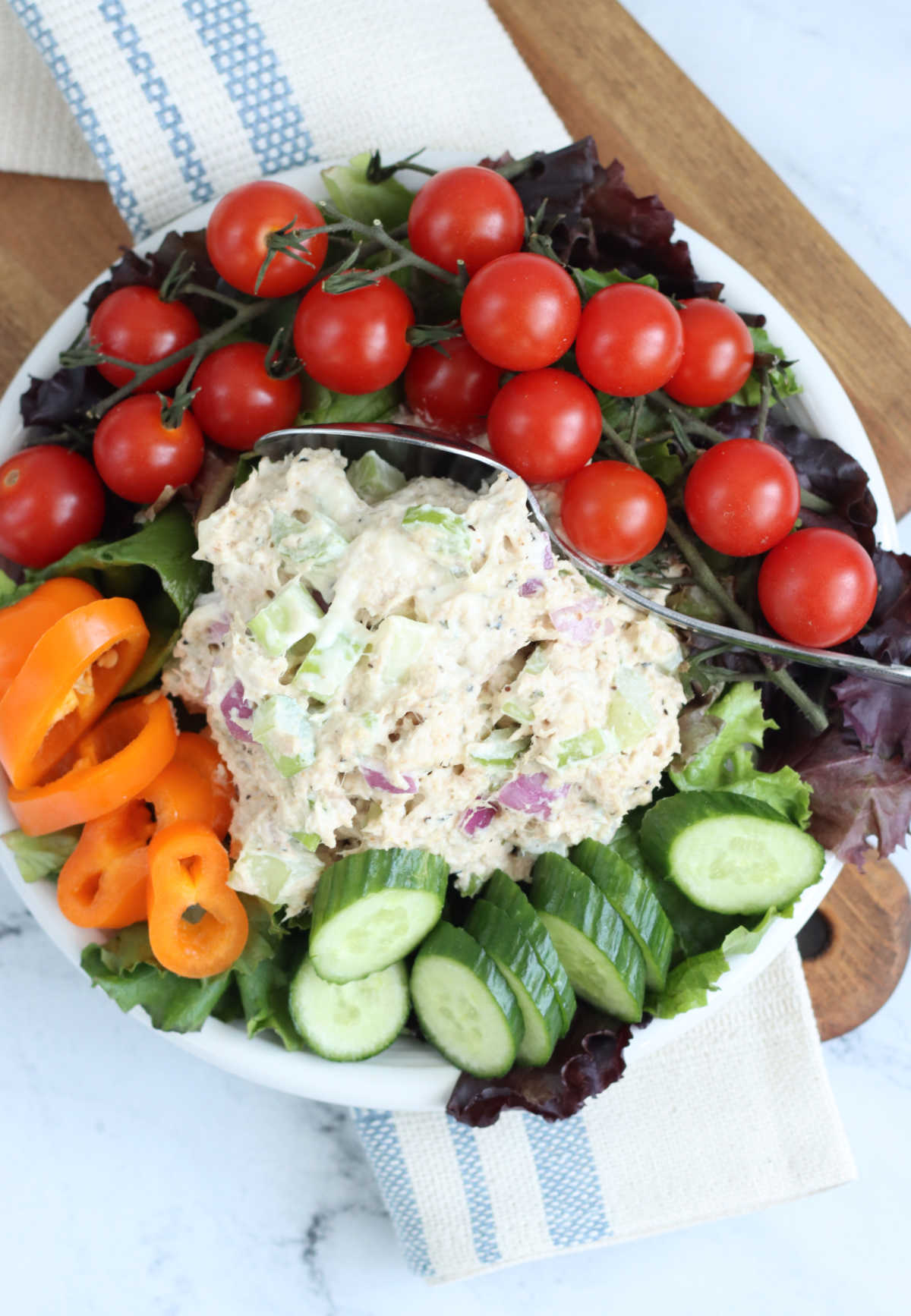 Scoop of tuna salad on small plate with cherry tomatoes, sliced cucumber, bell pepper and greens.