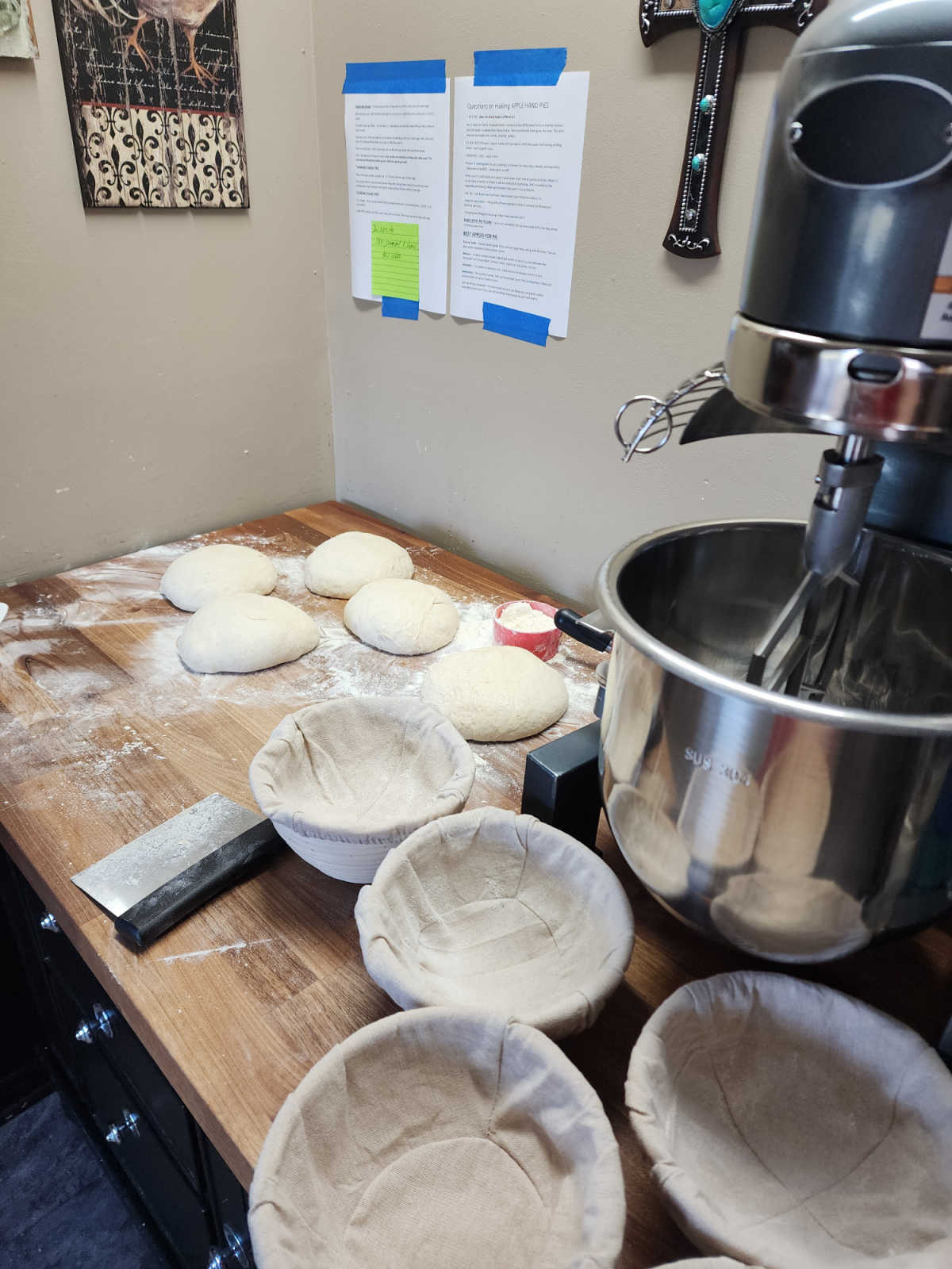 Dough on butcher block with small round bannetons, large stand mixer in background.