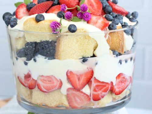 Berries, pound cake and pudding in trifle dish, topped with mint and small purple flowers.