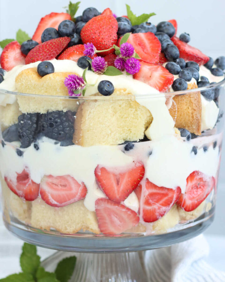 Berries, pound cake and pudding in trifle dish, topped with mint and small purple flowers.