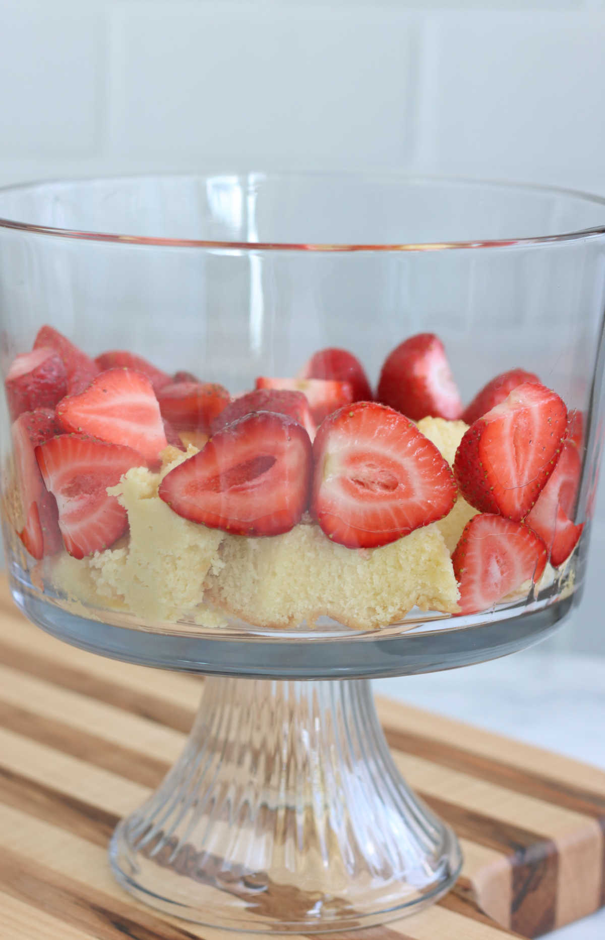 Layering strawberries and cake in clear glass trifle dish.