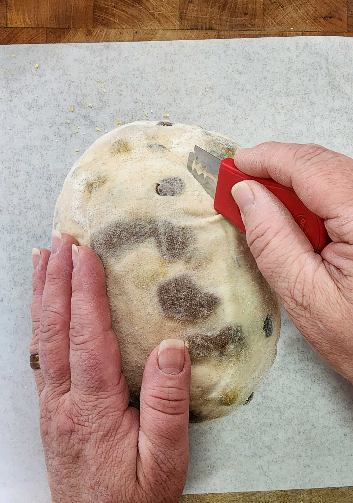 Hand holding red bread lame cutting into cinnamon raisin sourdough on butcher block.