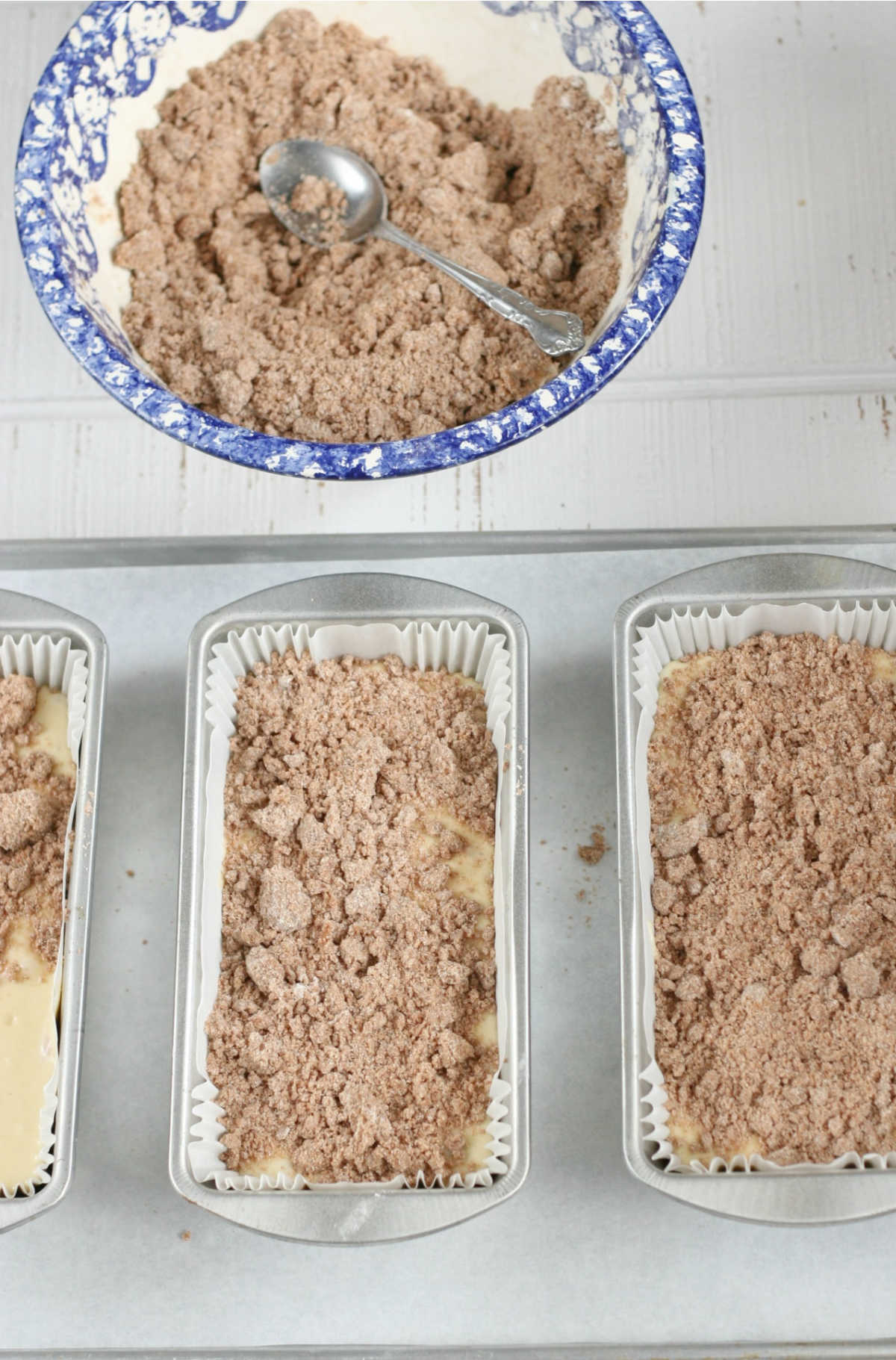 Coffee cake batter with crumb topping in metal loaf pans on half sheet pan.