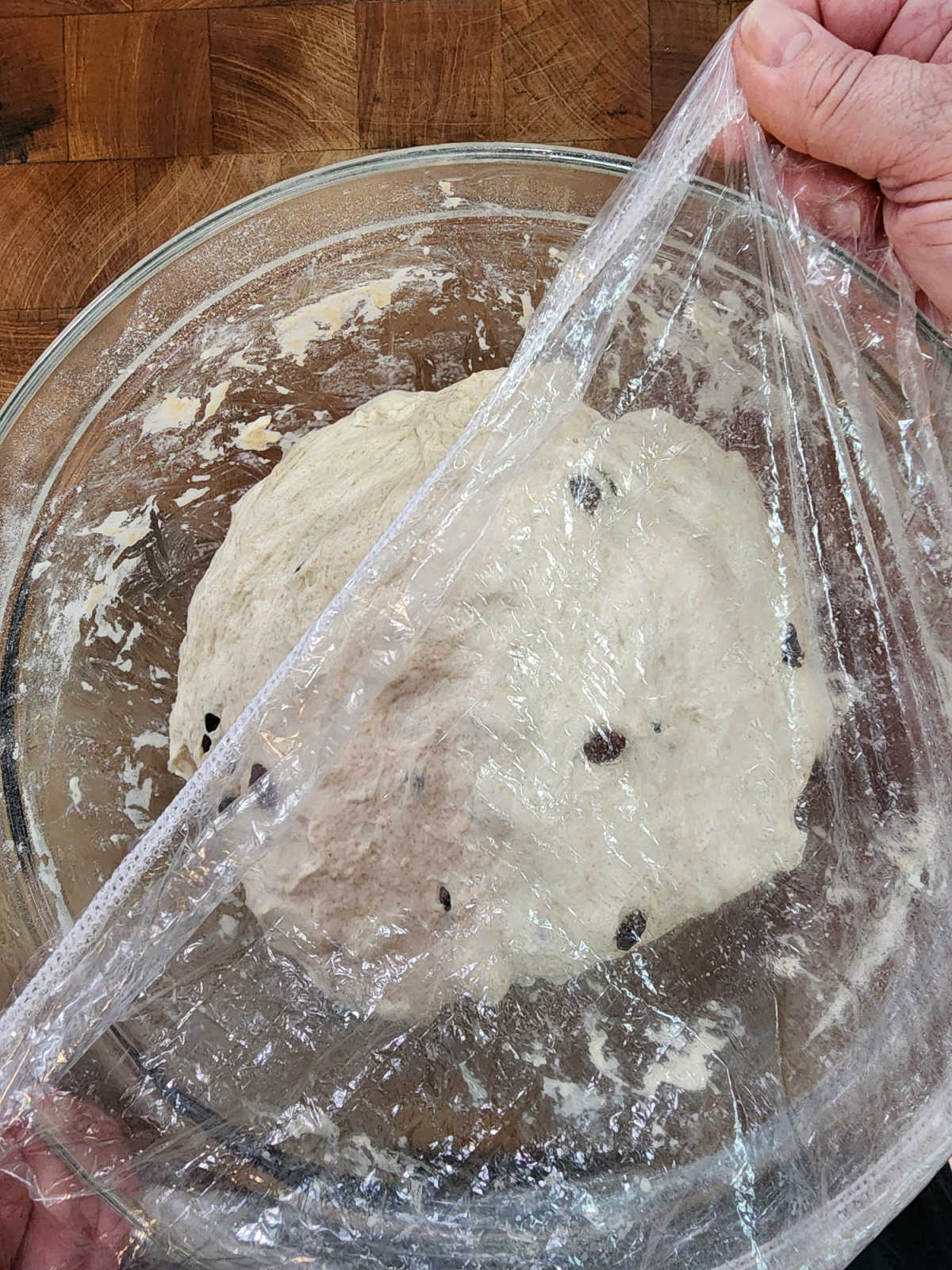 Covering clear glass bowl of sourdough dough with reusable shower cap.