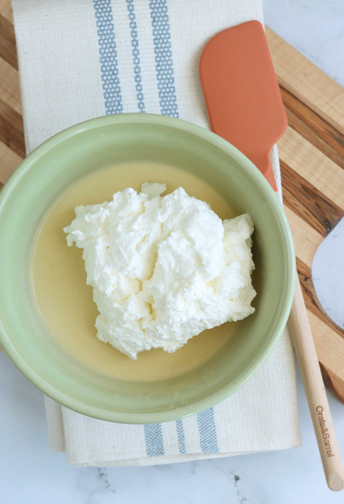 Pudding and whipped cream in pale green mixing bowl on wooden cutting board.