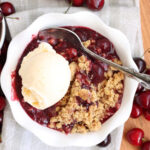Small white bowl with cherry crisp and vanilla ice cream.
