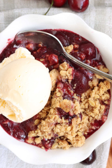 Small white bowl with cherry crisp and vanilla ice cream.