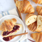 Sourdough croissant cut in half on small white plate with raspberry jam.