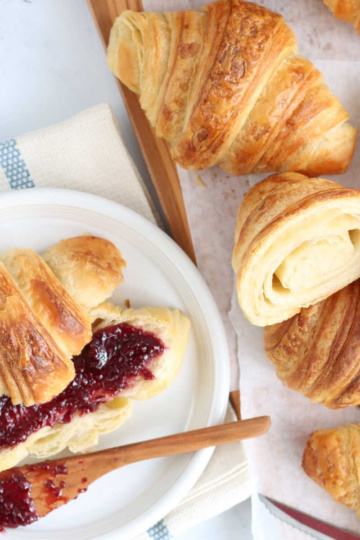 Sourdough croissant cut in half on small white plate with raspberry jam.