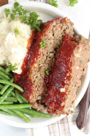 Two slices of meatloaf, mashed potatoes, green beans on small white plate.