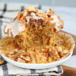Bite out of carrot cake muffin on small white plate.