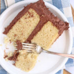 Slice of yellow layer cake with chocolate frosting on small white plate.