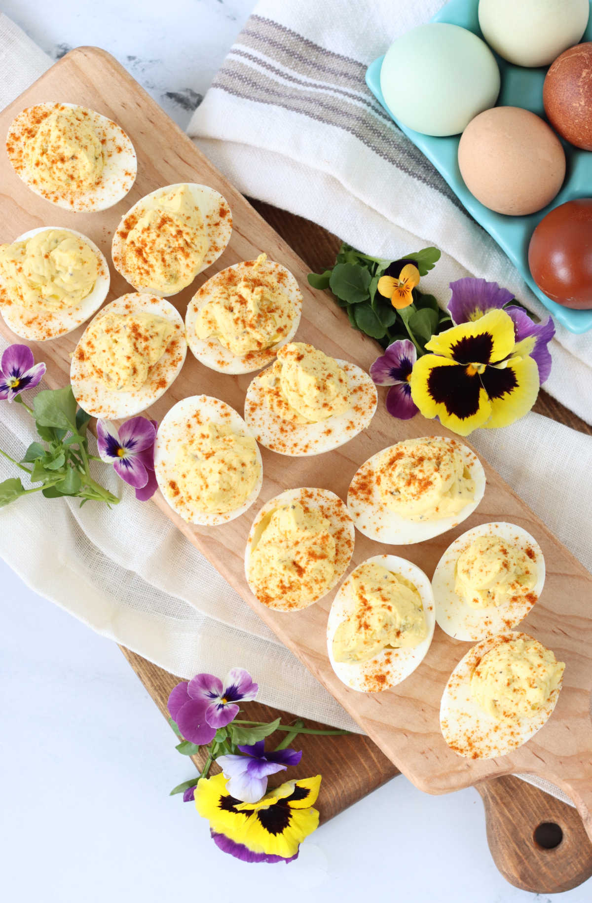 Deviled eggs with paprika on narrow wooden cutting board.