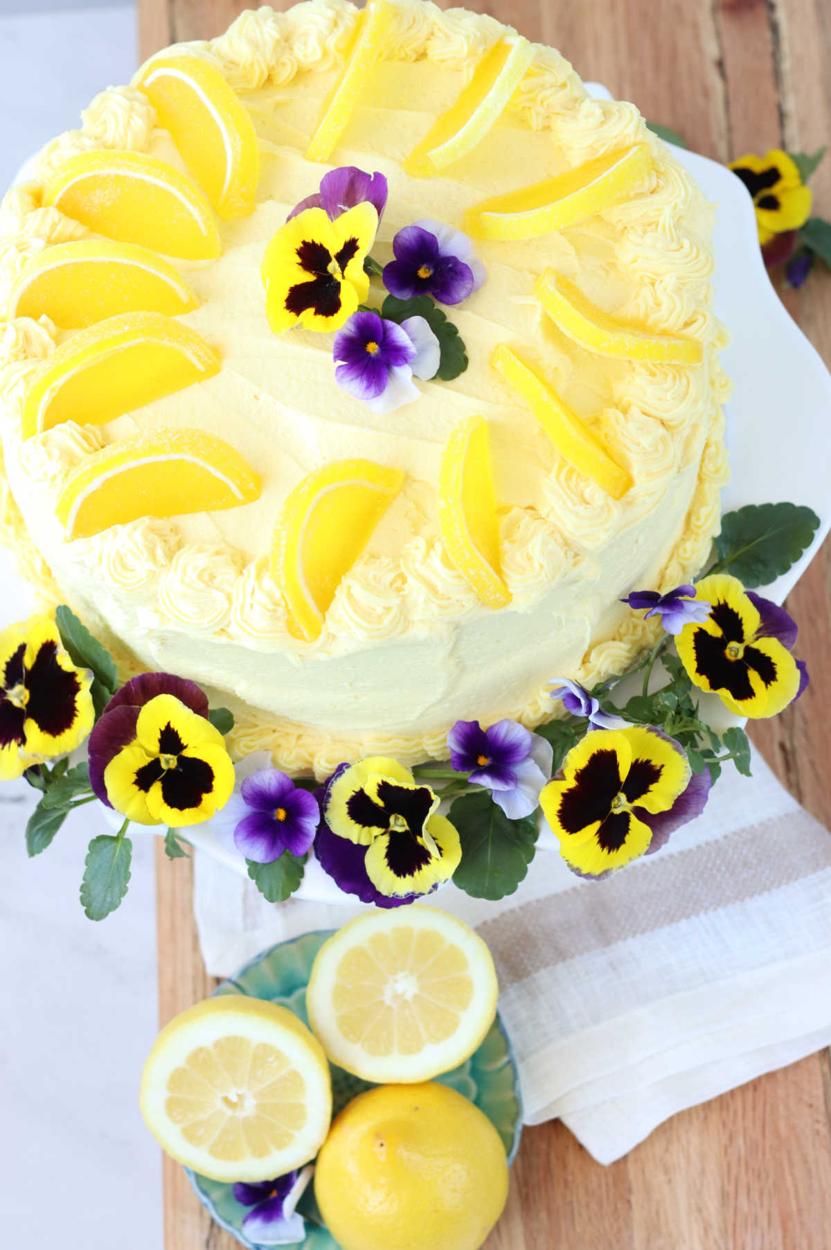 Overhead of lemon cake with lemon frosting, pansies and lemon candies on cake.