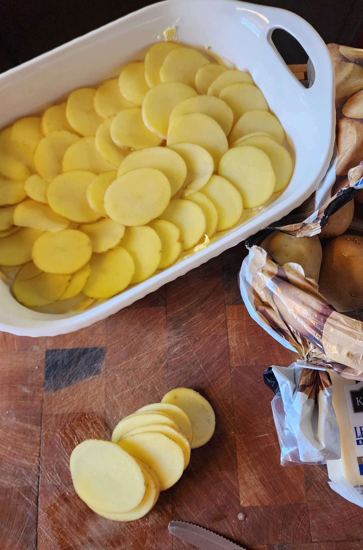 Slices of potatoes being placed into a white baking dish.